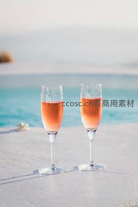 两杯桃红起泡酒静置泳池边，碧海蓝天映衬下尽显度假奢华感
