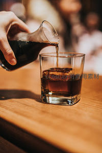 琥珀色威士忌缓缓注入冰块玻璃杯，木质吧台映衬温暖光影
