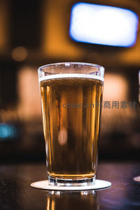 金黄啤酒满杯泛白沫，置于吧台杯垫上，背景电视屏光晕朦胧