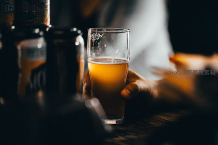 手持冰镇啤酒杯，泡沫轻溢，吧台暖光映衬朦胧氛围