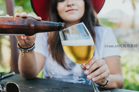 女子户外手持酒瓶倾倒金黄啤酒入高脚杯，泡沫细腻，氛围惬意