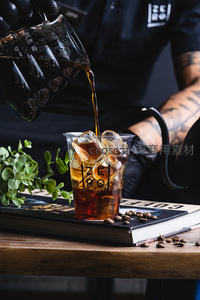 咖啡师戴黑手套精准手冲冷萃咖啡，冰块晶莹，书本与绿植点缀木质台面