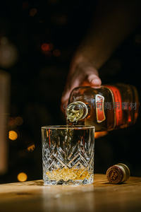 琥珀色威士忌倾倒入雕花水晶杯，暖光映衬醇厚质感