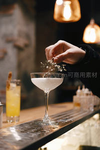 调酒师手撒满天星点缀白色鸡尾酒，暖光吧台氛围感十足