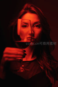红光映照下女子手持红酒杯，镜面折射面部，神秘氛围肖像
