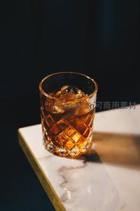菱格纹威士忌杯盛琥珀色酒液与冰块，大理石台面反光精致