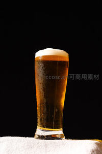 黑底映衬冰凉啤酒杯，泡沫绵密水珠凝结杯壁