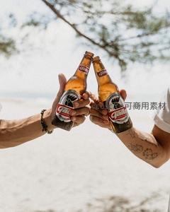 海滩上两人举杯碰击嘉乐啤酒，树影洒落沙岸