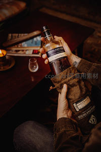 手握Highland Park威士忌酒瓶与麻布袋，暖光烛影下的品鉴时刻