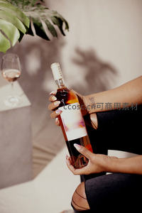 女性手持桃红葡萄酒瓶，绿植阴影映衬下的时尚品酒瞬间