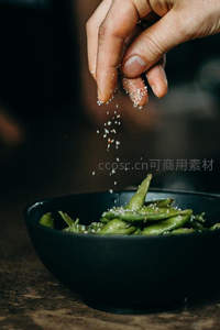 手撒海盐于青豆荚，暗调微距呈现烹饪瞬间