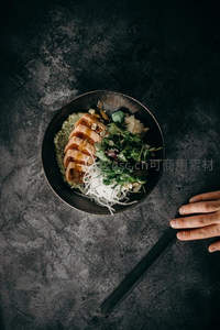 深灰石板背景上的日式拌饭碗，手握筷子俯拍构图