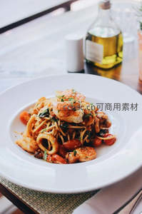 海鲜意面盛于白盘，虾仁鱿鱼配橄榄油瓶窗边光影