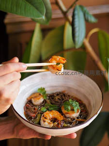 手握筷子夹起烤虾荞麦面，绿植背景下的亚洲风味轻食