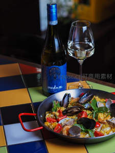 海鲜烩饭配白葡萄酒，色彩斑斓瓷砖桌上静物美食摄影