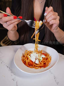 红指甲女性用叉勺卷起意面，番茄奶油意面配马苏里拉奶酪特写