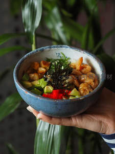 手捧蓝釉陶碗鲜虾牛油果沙拉，海苔碎点缀绿植背景