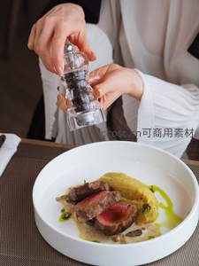 白瓷盘中煎牛排配土豆泥与黑胡椒研磨，女士手部特写