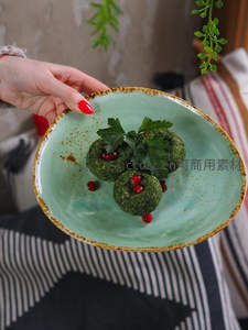 手托青釉粗陶盘，盛三颗绿色香草丸子配石榴籽与欧芹，居家氛围温馨自然