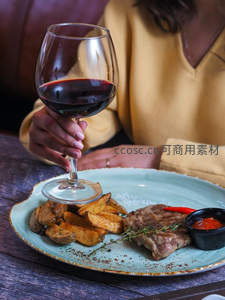手持红酒杯配烤牛排薯角，青釉盘盛装，温馨黄衣女子享受晚餐时光