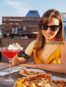 金黄吊带裙女子为红色鸡尾酒淋橄榄油，屋顶露台享受夏日微醺时刻