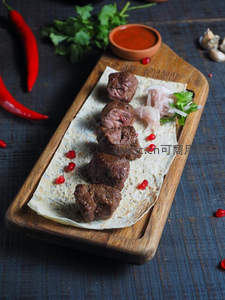木质托盘上的烤牛肉串配薄饼，点缀石榴籽与洋葱丝，佐以辣酱与香草