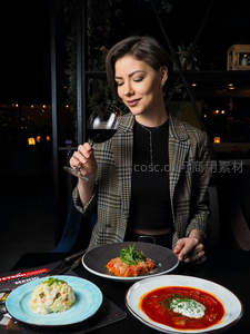 女士品鉴红酒，面前三道意式菜肴：千层面、俄式沙拉与番茄汤