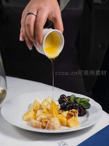服务员正将蜂蜜淋于水果沙拉，含苹果梨葡萄与核桃