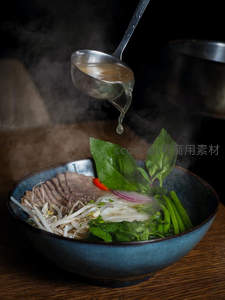 热气腾腾越南河粉特写，高汤正从勺中浇入配香草豆芽