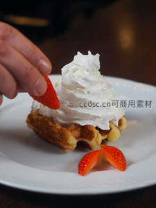 手捏草莓点缀奶油华夫饼的甜点特写