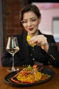 女士优雅挤柠檬汁点缀海鲜烩饭，搭配白葡萄酒，氛围温馨雅致