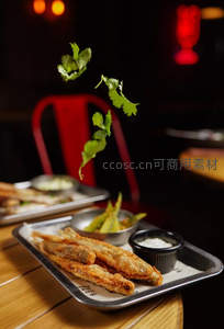 炸鱼条配蘸酱与飞舞香菜叶，动态抓拍营造食欲与活力感