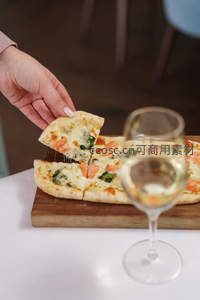 手取三文鱼菠菜披萨切片，配白葡萄酒杯与木质砧板
