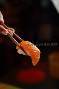 筷子夹起鲜嫩三文鱼寿司，橙红鱼肉纹理清晰，米饭紧实饱满