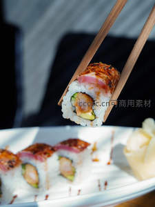 筷子夹起炙烧金枪鱼寿司卷，米饭饱满，内馅清晰可见