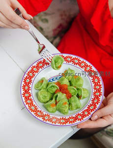 红裙女子用叉取绿色饺子，配鱼子酱，花纹瓷盘色彩鲜艳