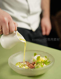 厨师正将金黄色酱汁缓缓淋入精致沙拉碗中，呈现高级料理的优雅瞬间