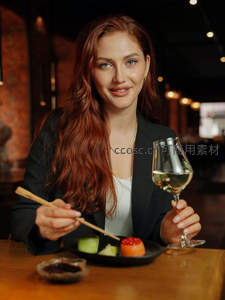 黑西装女子持酒杯微笑，搭配寿司与筷子，优雅品鉴日料