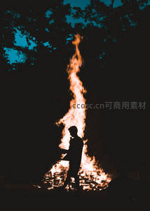 夜幕下篝火旁的人影剪影，火焰升腾映衬深蓝树影