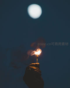 夜空下手持烟花棒，月光朦胧映衬微光烟雾袅袅升腾