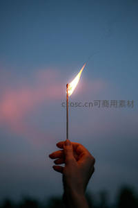 暮色中手持燃着的火柴，细小火焰在渐变天幕下轻舞，烟迹袅袅升腾