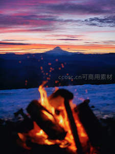 雪山日落前篝火映照，远山剪影与霞光交织壮丽景致