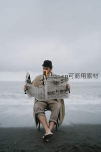 黑沙滩上男子持燃烧报纸阅读，海风拂面孤寂又超现实