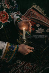 民族风刺绣衣袖托举烛台，暖光映照繁复纹样地毯，静谧庄重