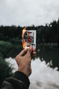 手持燃烧的黑桃J扑克牌，背景湖林朦胧如梦