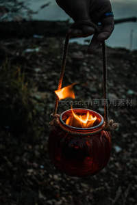 暮色中手提玻璃油灯，火焰摇曳映照粗绳与陶罐