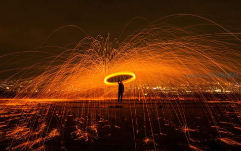 钢丝棉光绘夜景，人影持环挥洒橙红火花，城市灯火为幕