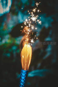 烟花棒喷射星芒火花，蓝绿虚化背景下的节日瞬间