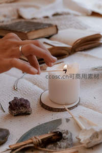手点燃白色蜡烛，搭配紫晶、古书与天然布艺的静谧仪式感场景