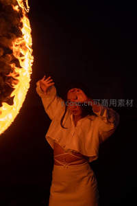 女子夜幕下以手遮光凝望巨大环形火焰，暖光映照白衣剪影